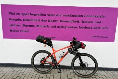 Fahrrad angelehnt an einer Wand mit aufgemaltem Zitat von Wilhelm Busch